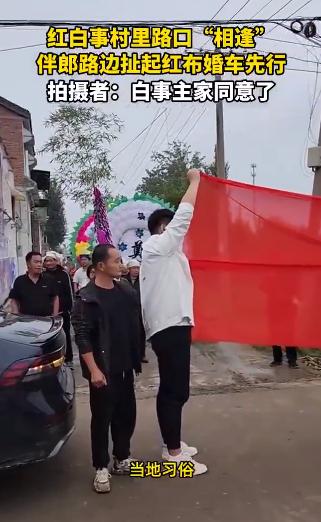 农村路口，婚车队伍和白事队伍意外遇上，场面看着就很微妙。
按照当地的做法，伴郎在