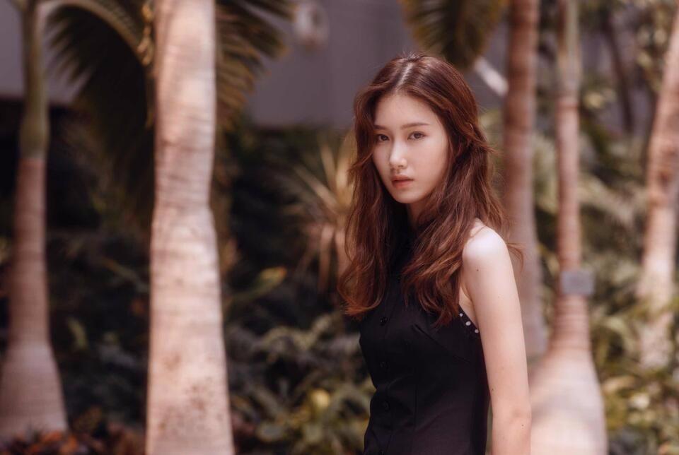 一个长发女孩站在热带植物前。