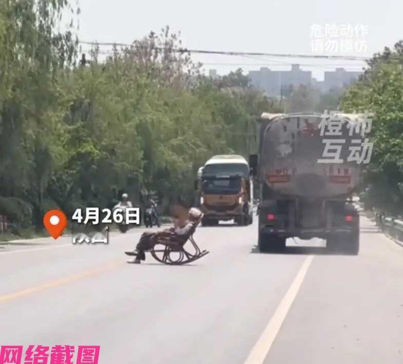 陕西有位大爷在忙忙碌碌的马路中间，一个人手里拿着折扇，身子躺在摇摇椅子上，看似晒