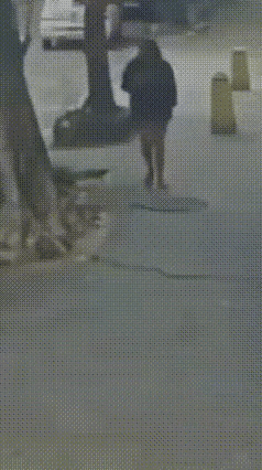 路上有一处老旧井盖，长期缺少维护已经松动。一名女子走路低头刷手机，一脚踩上去，井