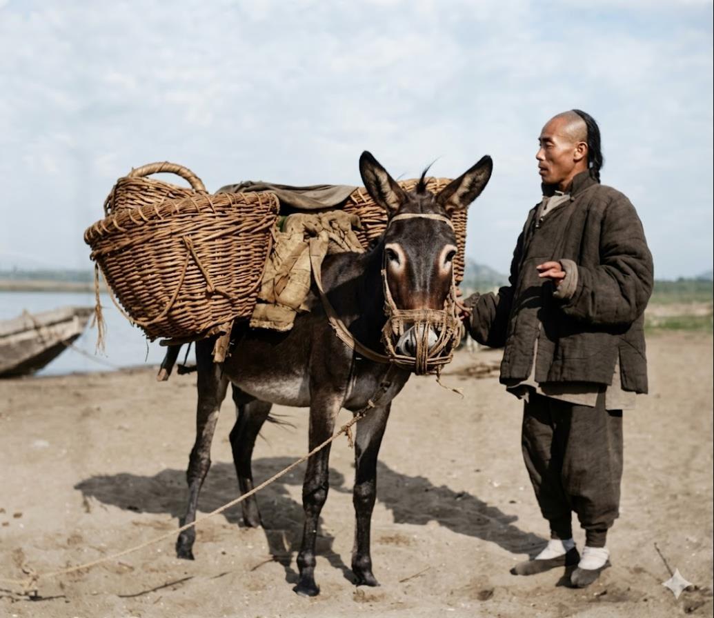 清末，河滩渡口，一个靠毛驴驮货谋生的乡间脚夫，男子身着粗布棉袄、宽松长裤，白布袜