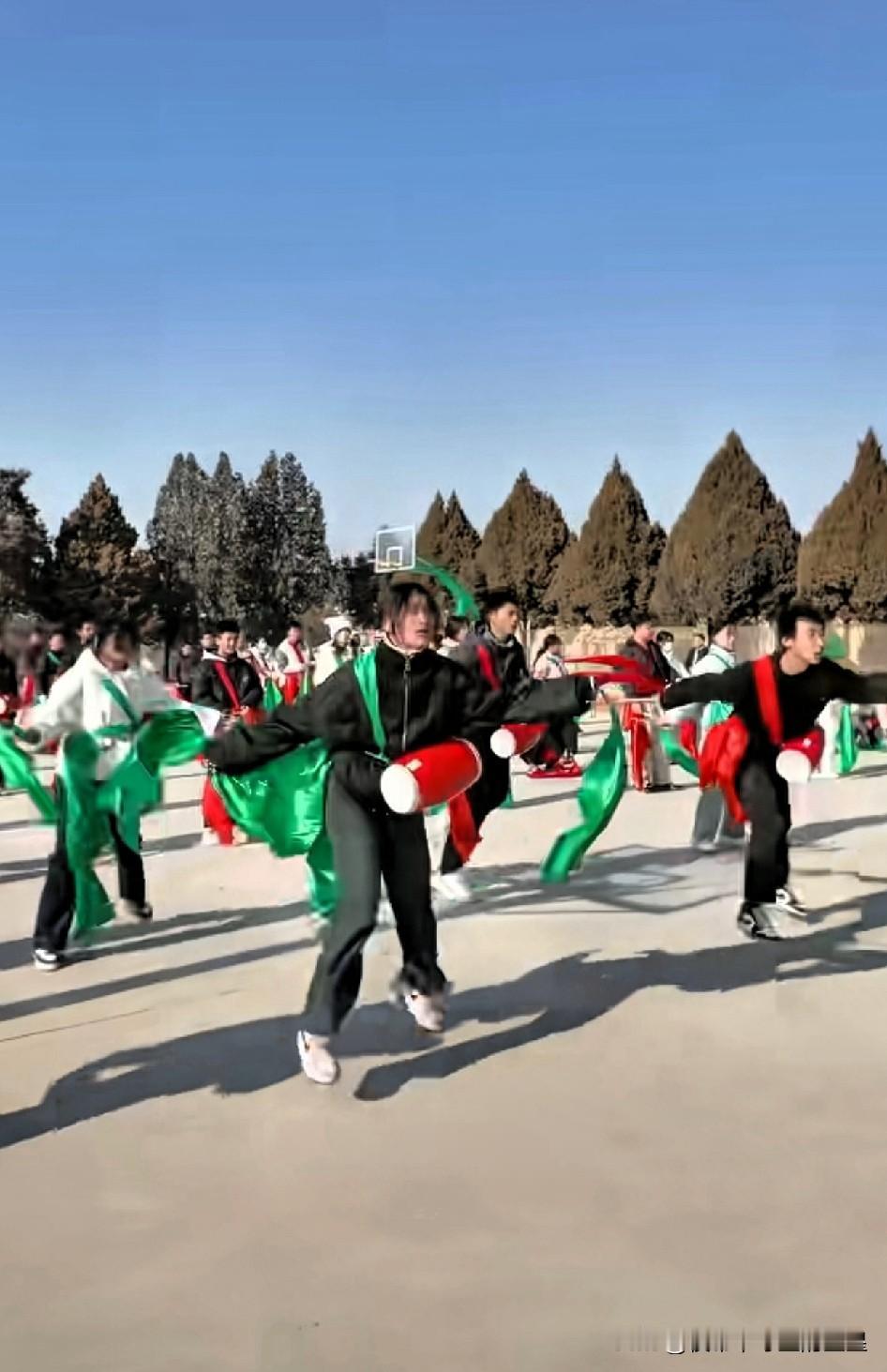 你看这广场上的阵仗——红鼓配绿绸，一群年轻人甩着彩绸蹦得那叫一个欢！鼓点一敲，彩