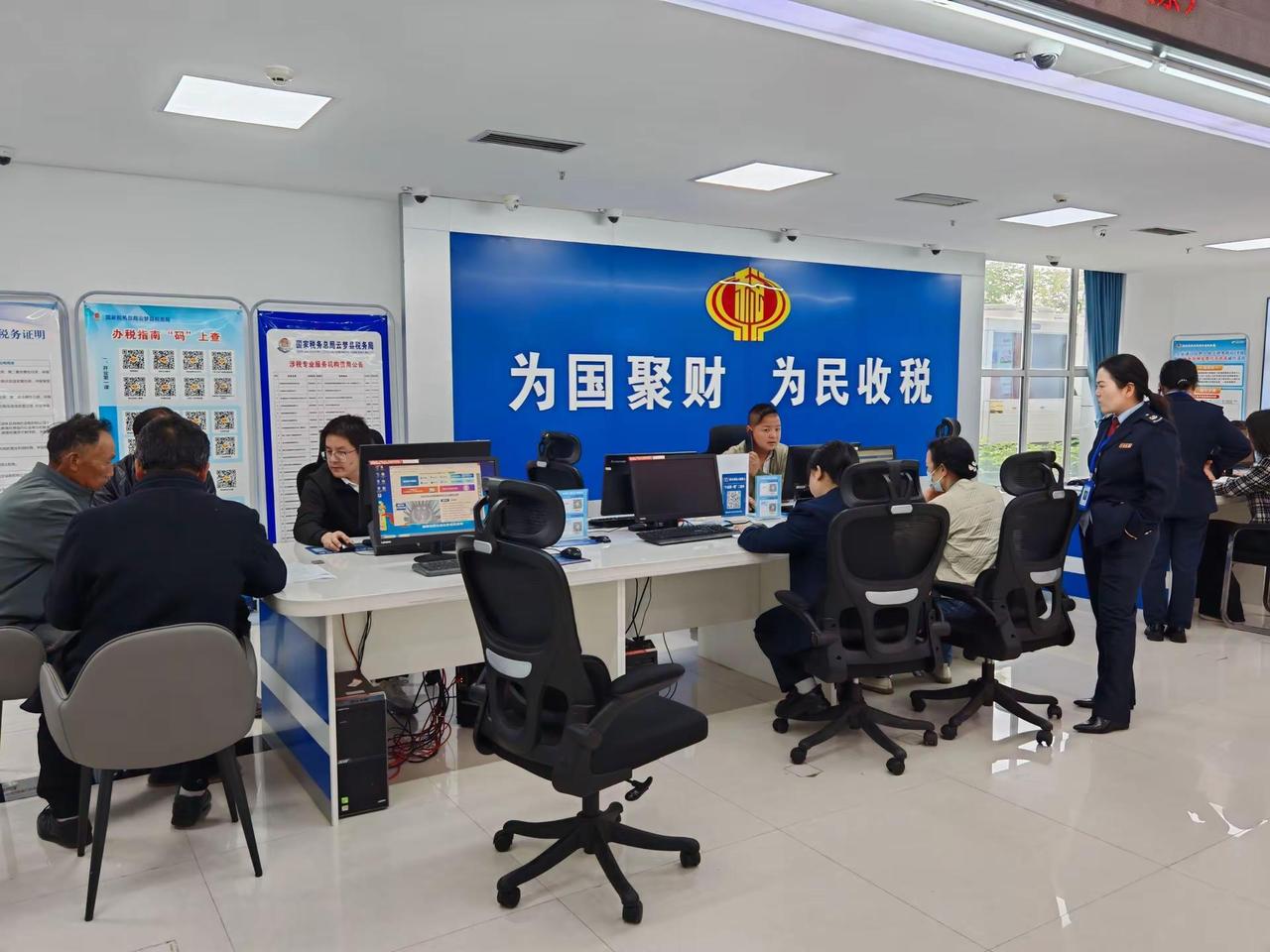 为国聚财  为民收税。在繁忙的窗口前，人们有序地办理业务，蓝色的背景板上写着“为