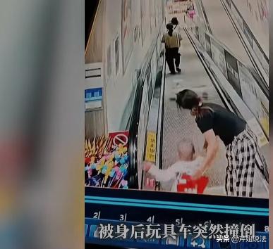云南，一宝妈抱着五个月婴儿坐下行扶梯，身后一名女子将玩具扭扭车放在扶梯上，扭扭车