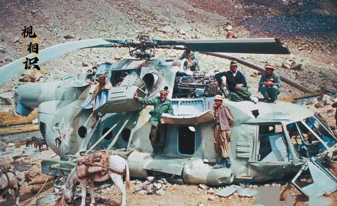 1988年，阿富汗山区，一架被击落的苏军米-8直升机残骸，几名游击队员兴奋地站在...