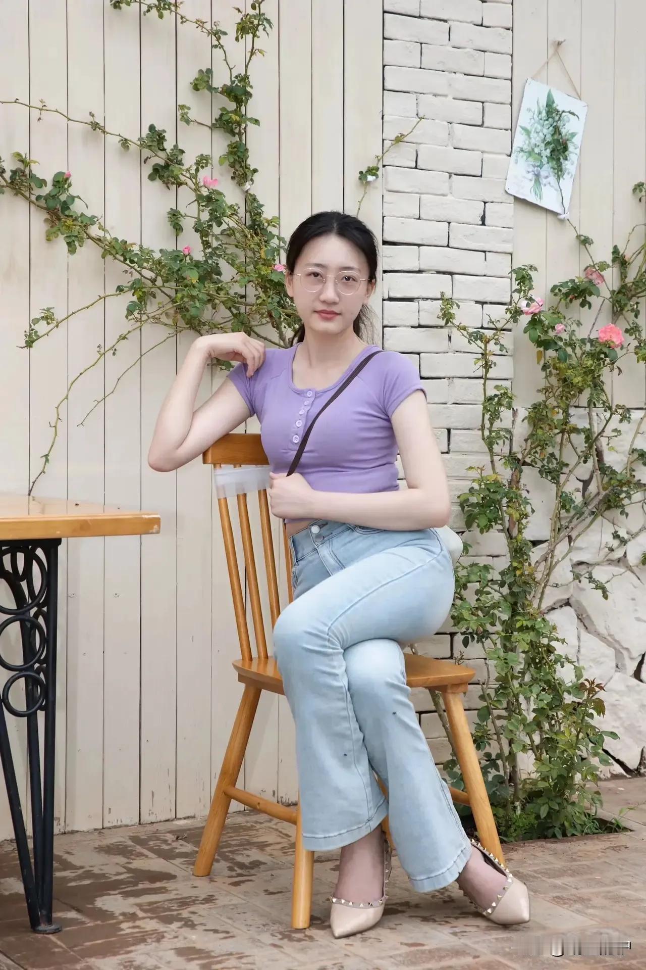 这位小姐姐坐在椅子上，穿着紫色上衣和牛仔裤，背景是花墙。分享你见闻过的绝色美人！