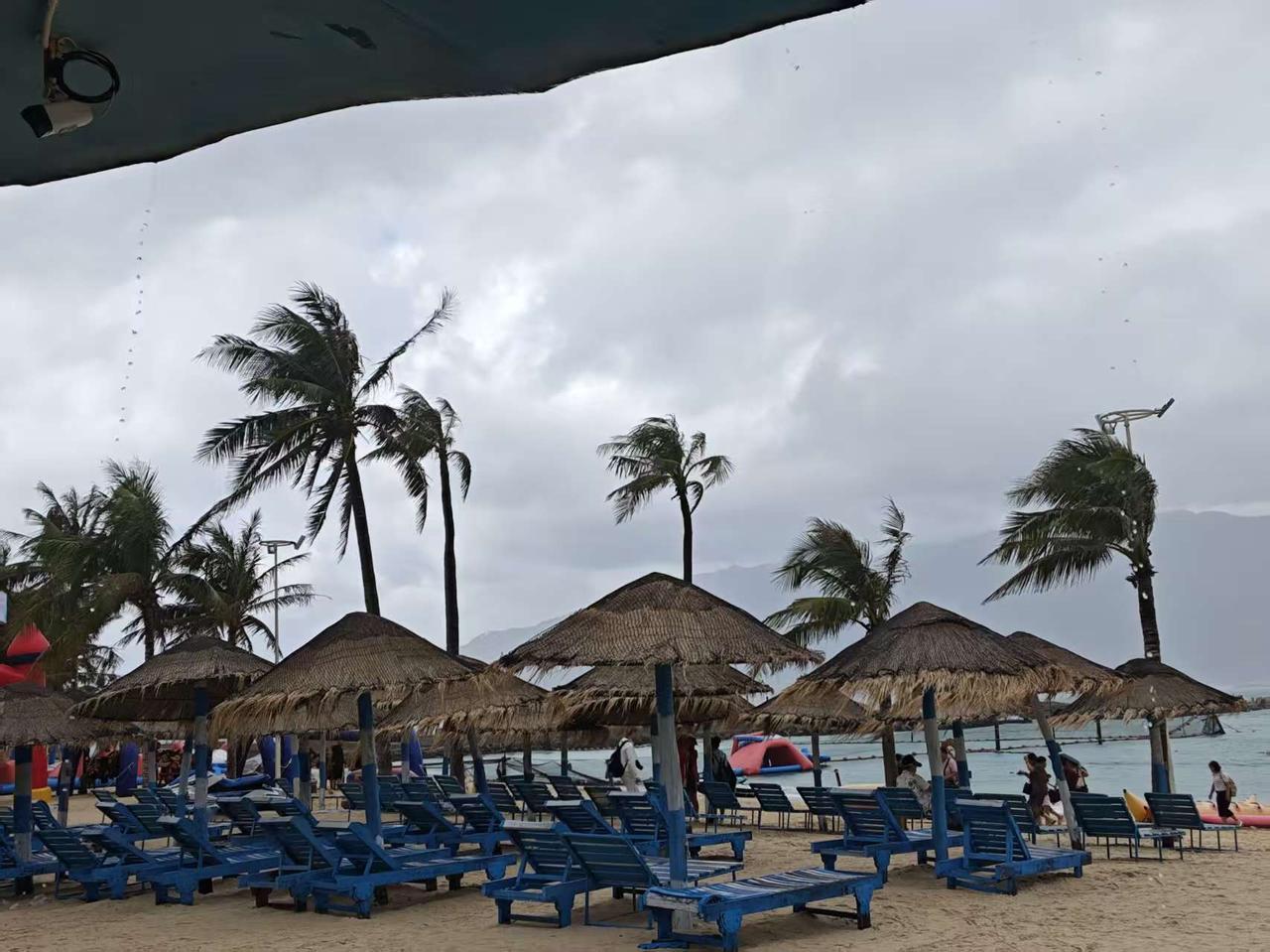 🌴 阴天的海边也有松弛感，椰树在风里轻轻晃，草伞下的躺椅等着收留放空的情绪。不