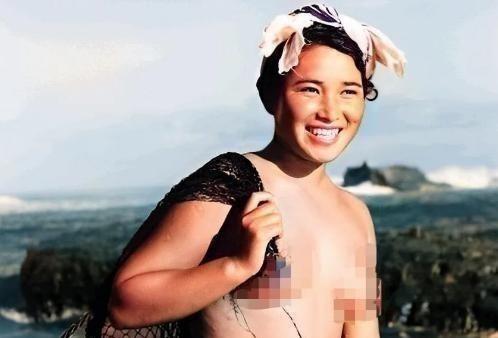1955年，一名身体强壮的日本女人赤裸上半身，背着一个黑色的编织袋站在海边。这个