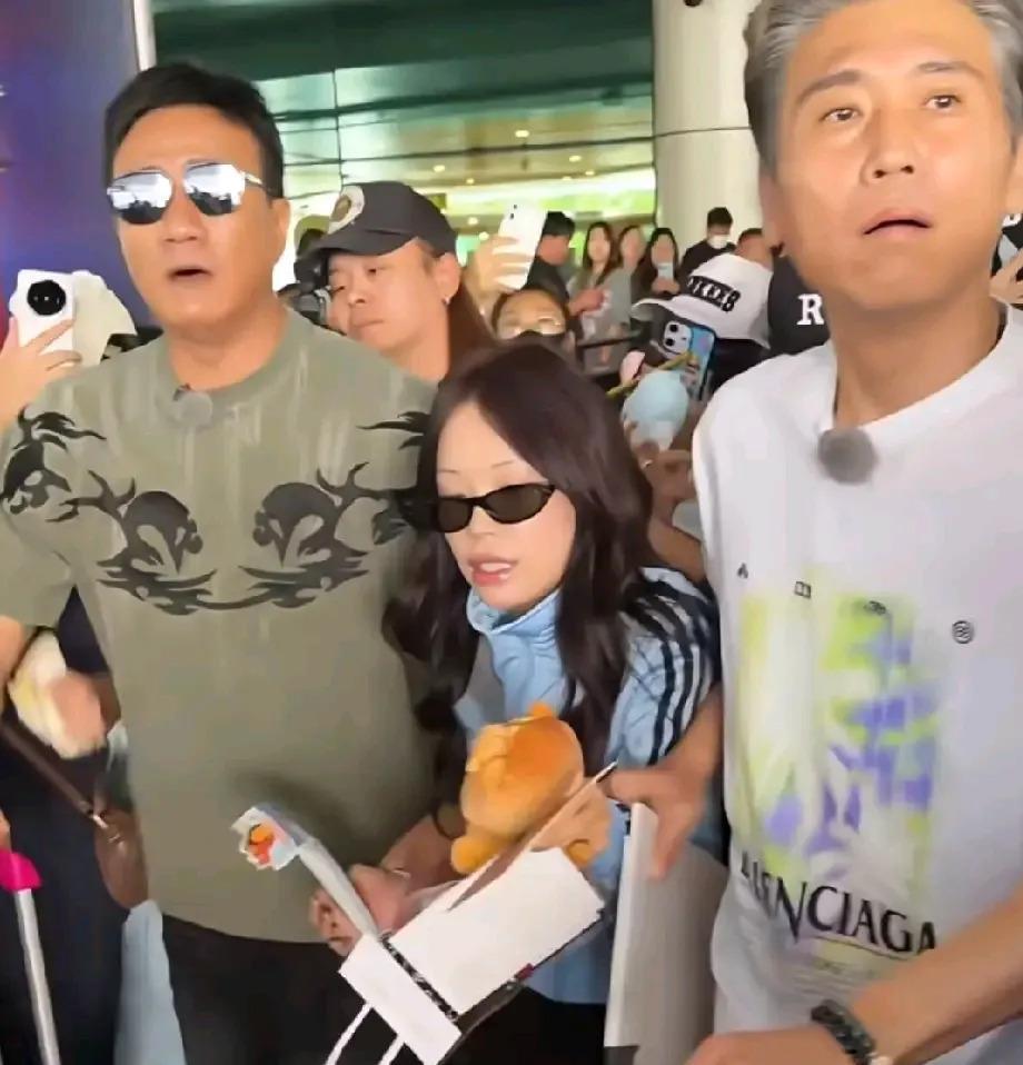 大连周水子机场，胡军和李乃文一左一右，把万妮达夹在中间往前走。 两个身高一米八上