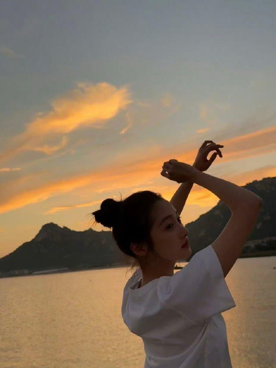 关晓彤的夕阳随拍好有氛围感！白T牛仔裤站在海边，身后是渐变的橘红晚霞，海风扬起发