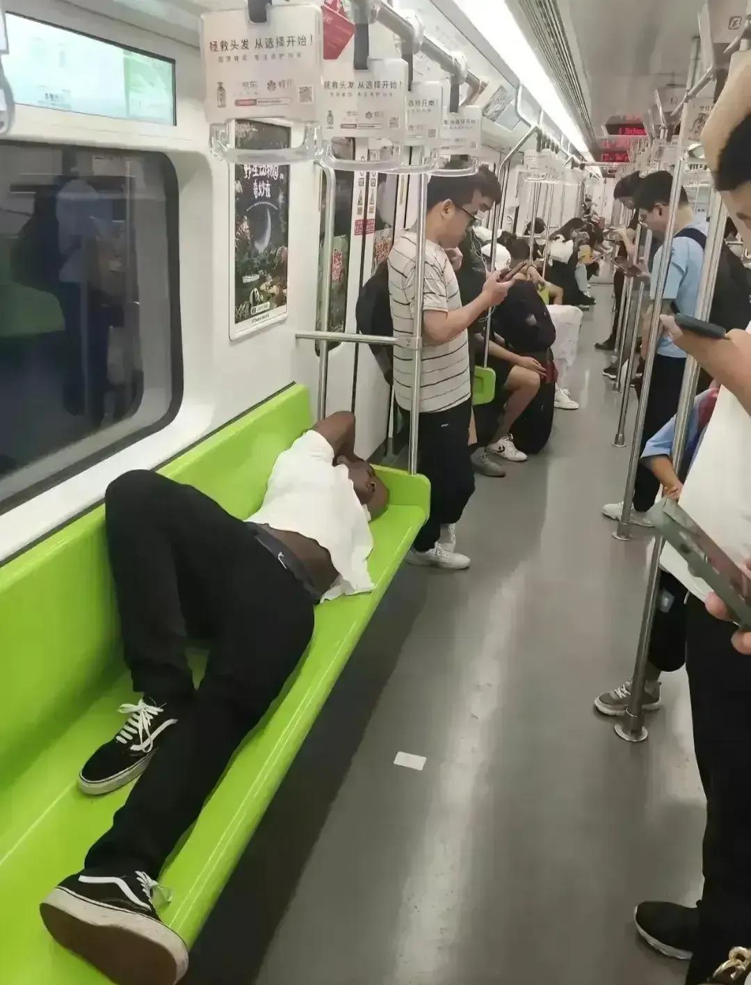 一群人站着，一个黑人躺在座位上，这是在非洲吗？看地铁的汉字，估计不是在非洲吧？如