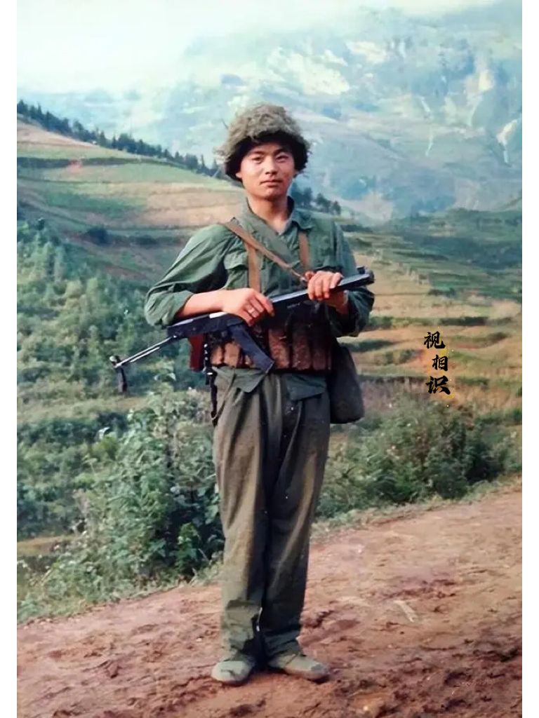 1985年，一等功臣周秋波的照片，画面中他身穿军装，戴着钢盔，手拿冲锋枪，显得英...