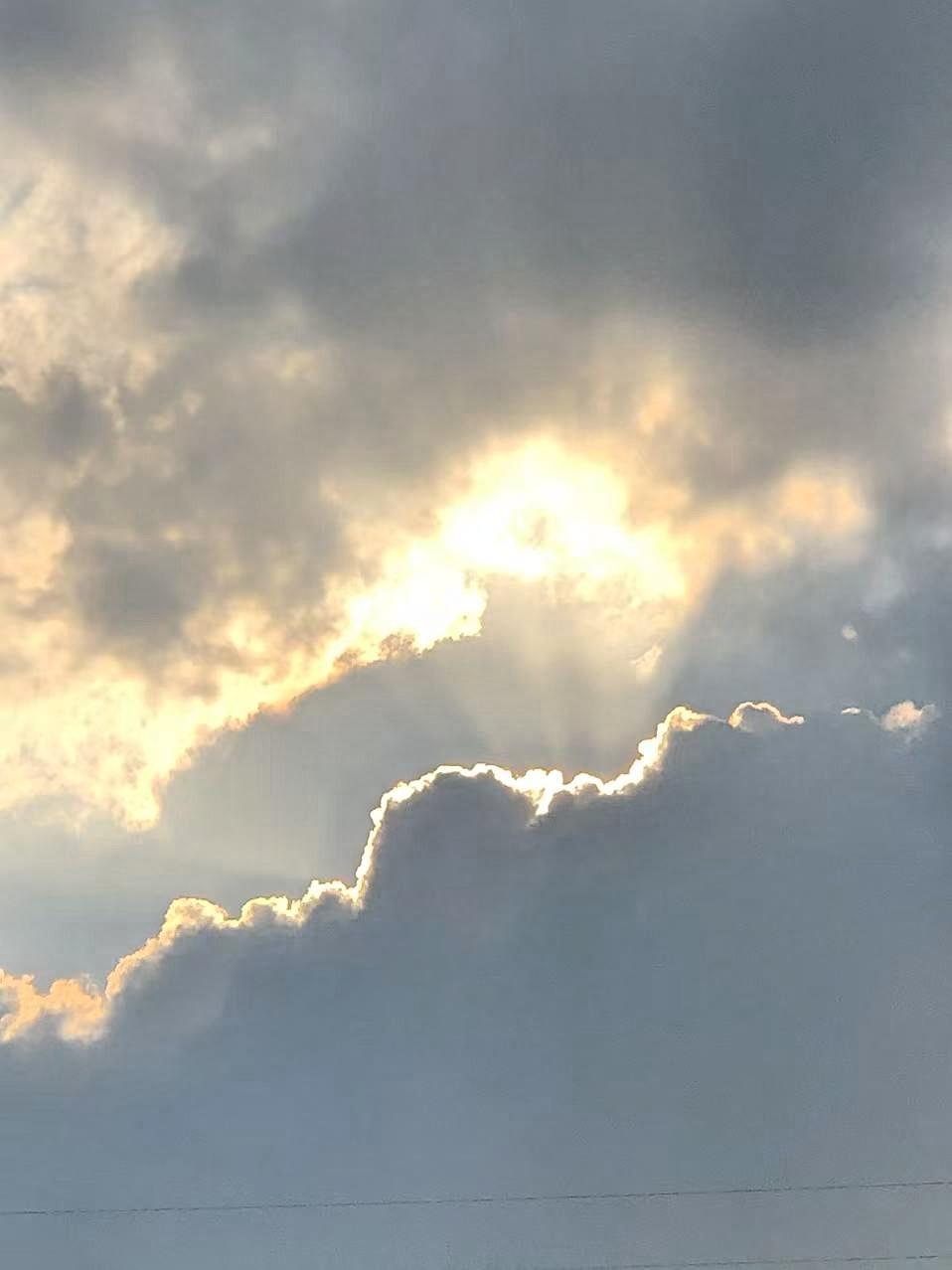 云层像被打翻的灰墨，却偏漏了几缕光。
 
日头藏在云后，把金边镶给云的轮廓，暖黄