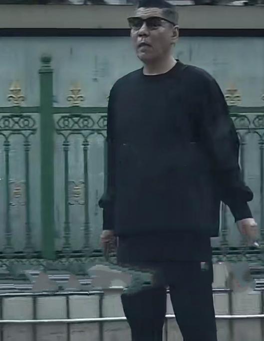 59岁屠洪刚在街边吸烟，他以前身形挺拔高大，身形健壮，头发乌黑浓密，戴着墨镜，虽