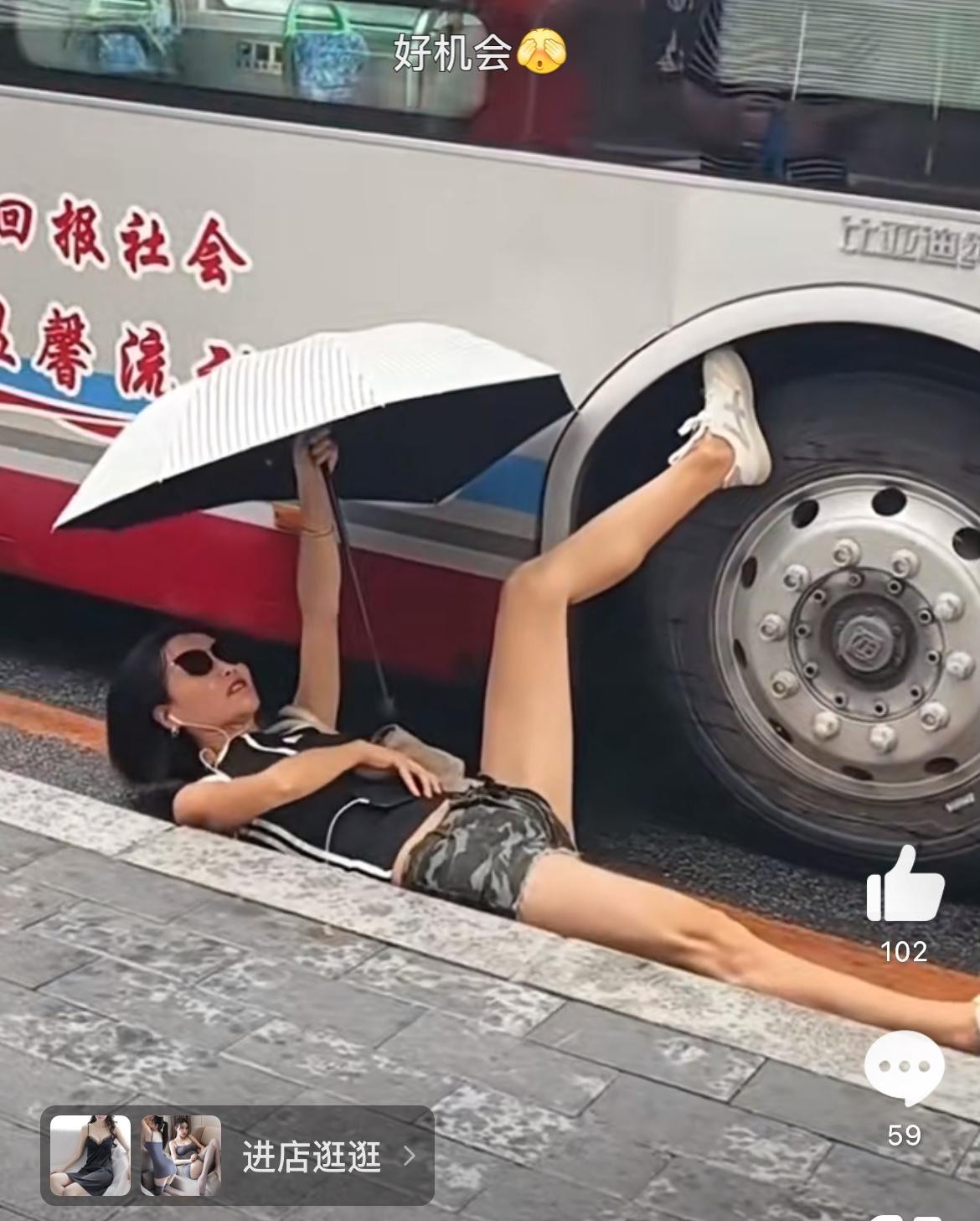 看姿势女子是和公交车杠上了。一只脚搭在公交的轮胎上，人躺在地上，关键是还撑着伞，