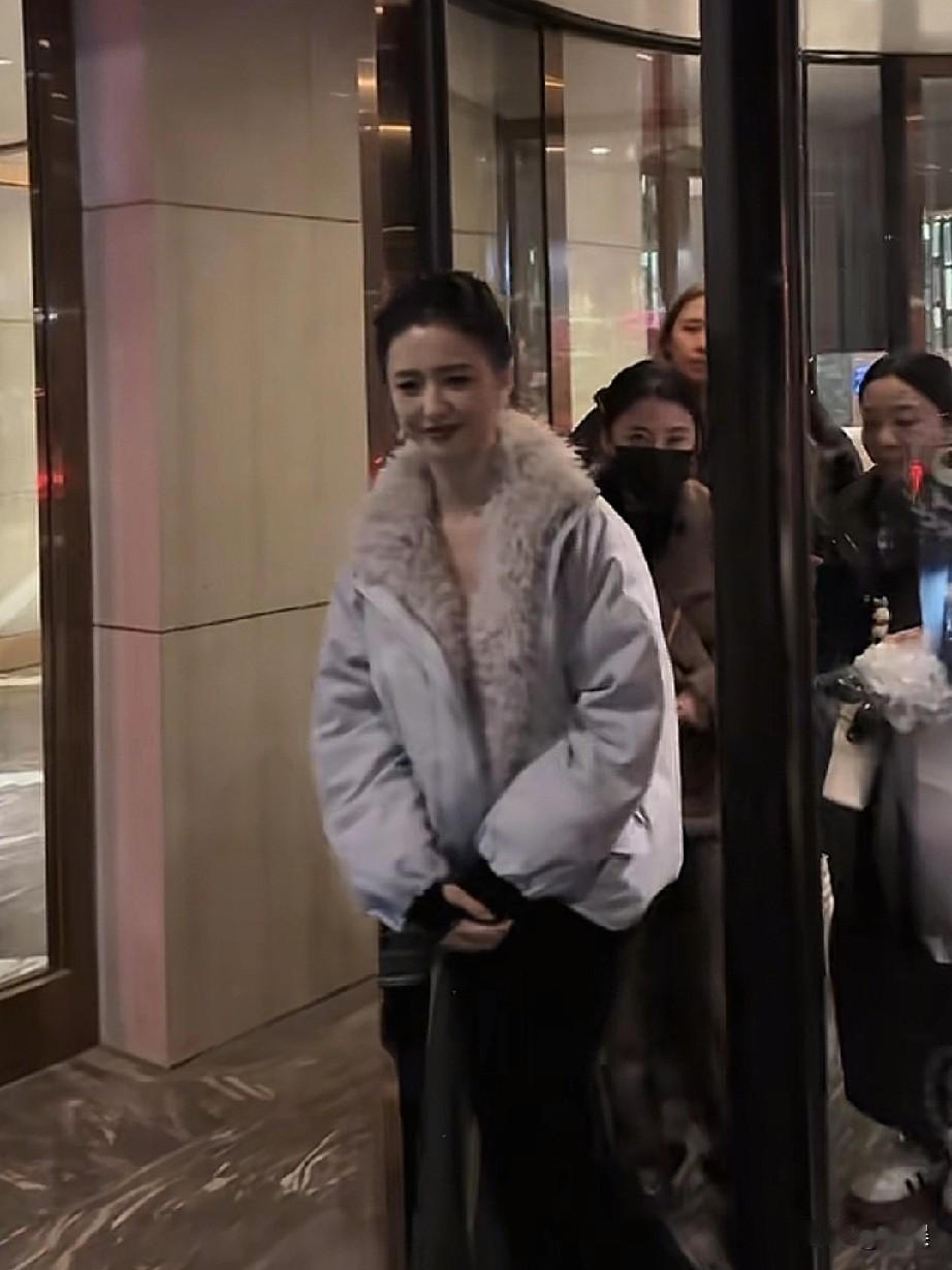 在旋转门旁，佟丽娅身着浅灰色带毛领的棉服