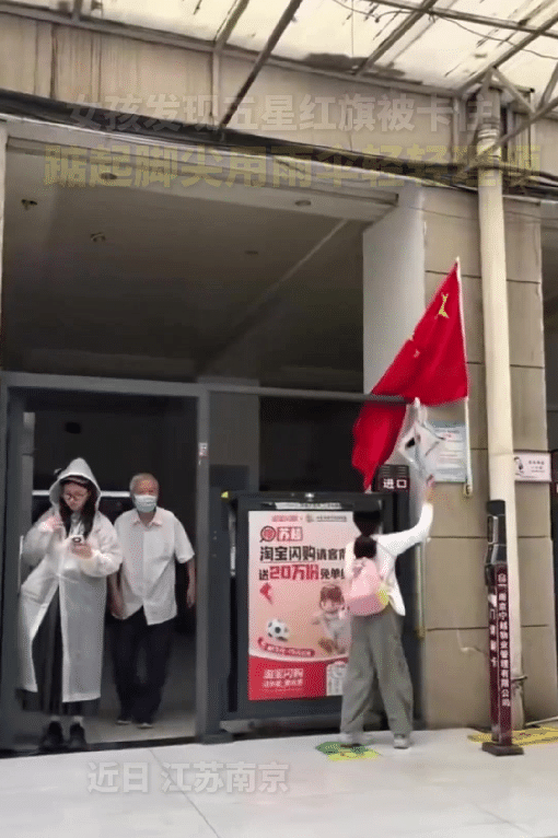 近日，江苏南京，一位女孩路过一处门口，发现悬挂的五星红旗被门卡住了，她停下脚步，
