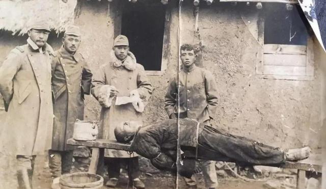 1935年，辽东-某地，破旧的土坯房前，一位抗联战士被牢牢绑在长凳上，手脚被缚，