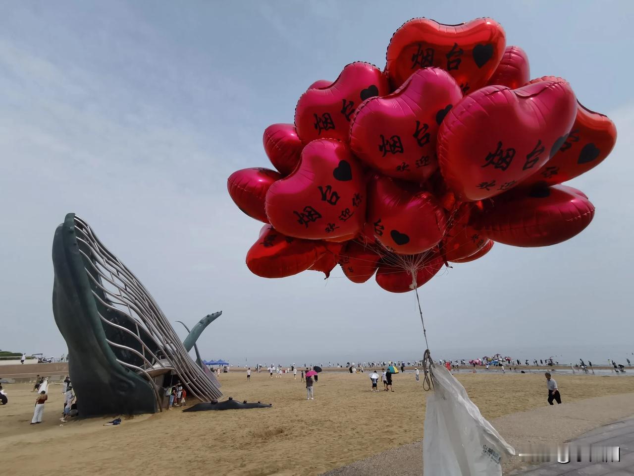 海鲸游浪影，人潮涌沙滩。
        山东省烟台市福山区金沙滩网红打卡点——