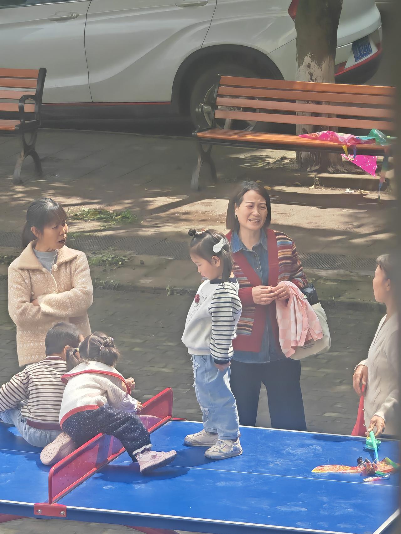 几个带娃的家长聚在一起吹牛，完全不管自家小孩在乒乓球桌上蹦蹦跳跳。那乒乓球桌可不