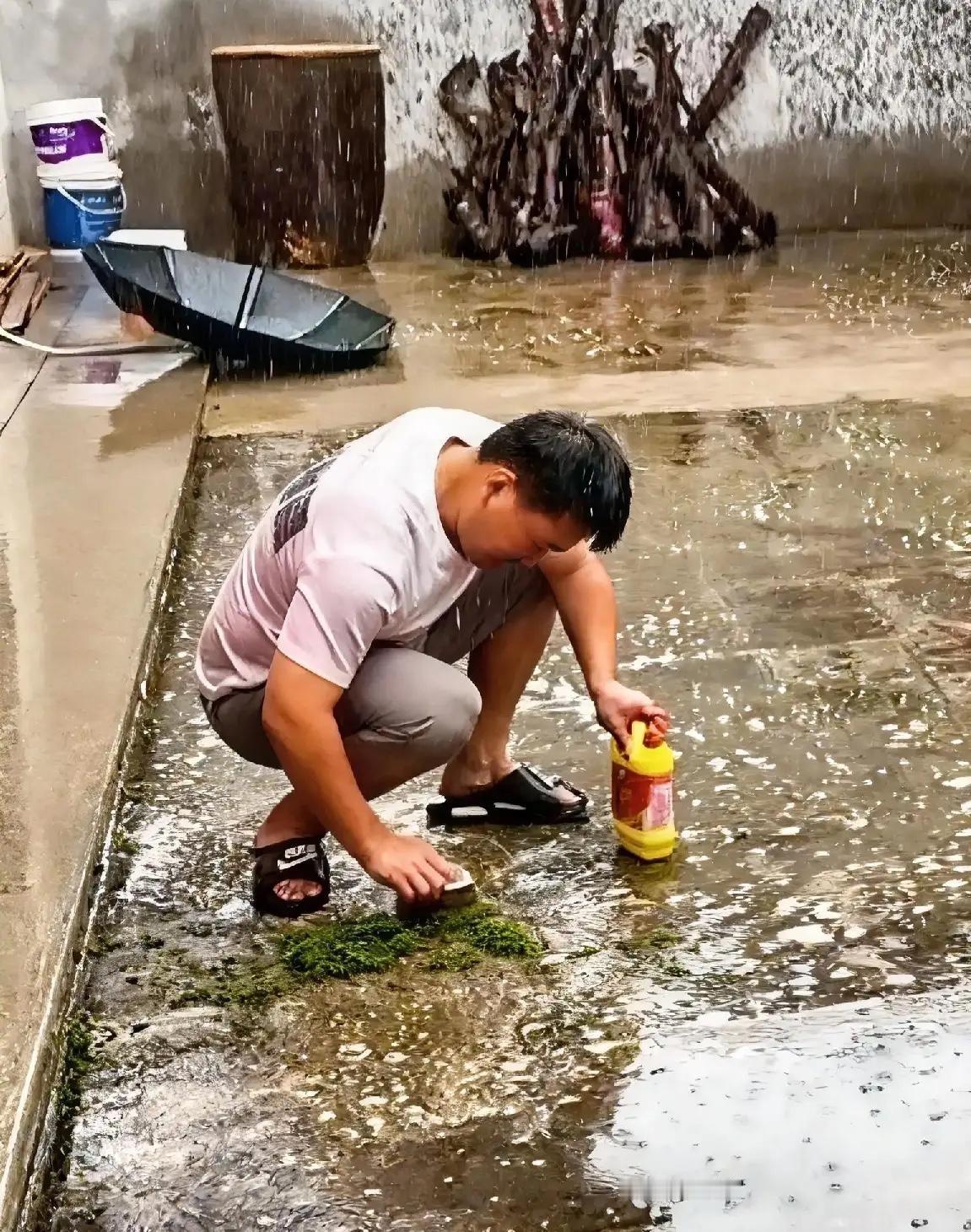 下着大雨，男子蹲在自家院子里，用刷子蘸着洗洁精，非常用劲卖力的在刷地面，衣服湿透