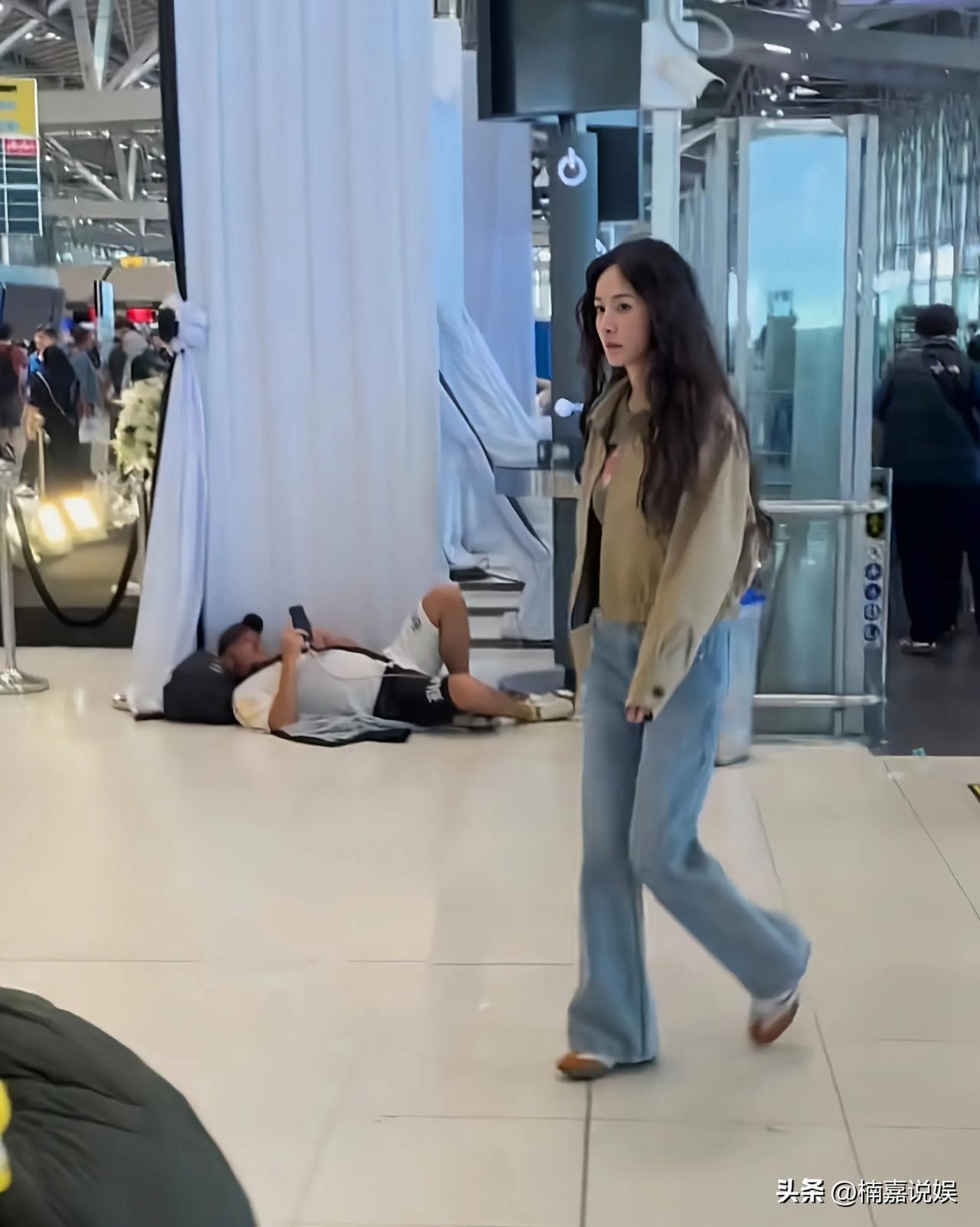 杨幂现身泰国，留一头长长的羊毛卷，穿着一件黄绿色短装外套配牛仔裤，脚踩平底鞋。