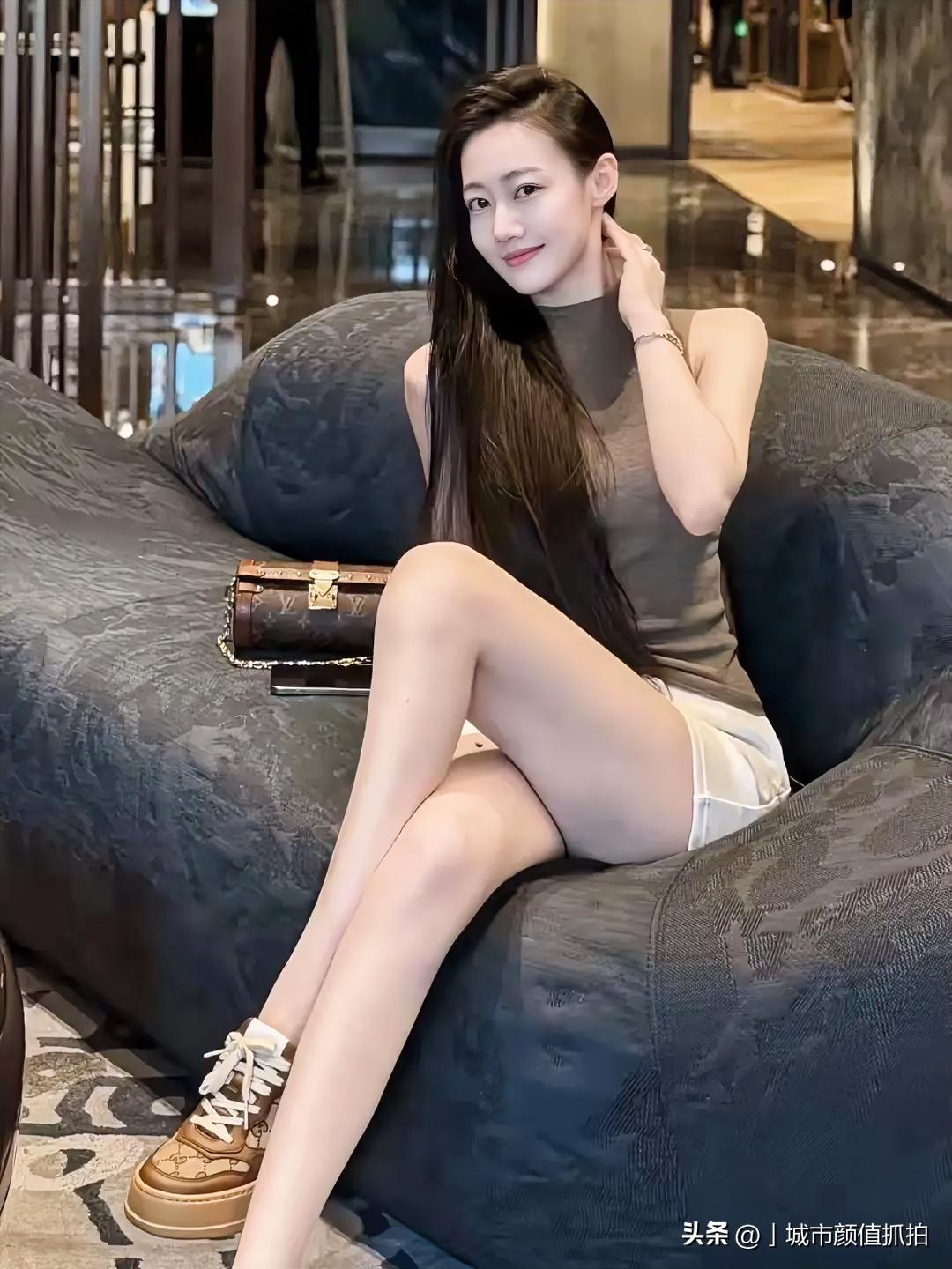 在酒店大堂的深灰沙发上随手落座，一身低饱和咖色无袖高领搭配简约白短裤，长发自然垂