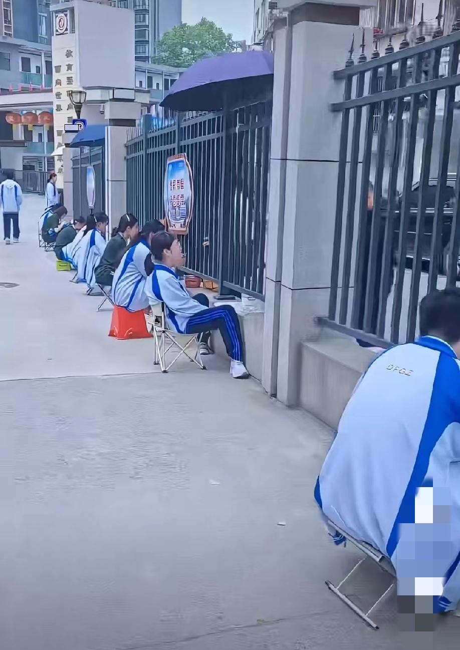 湖北十堰，网友上传的一段视频:中午时分，某学校围墙边，一长溜都是学生，各自坐在小