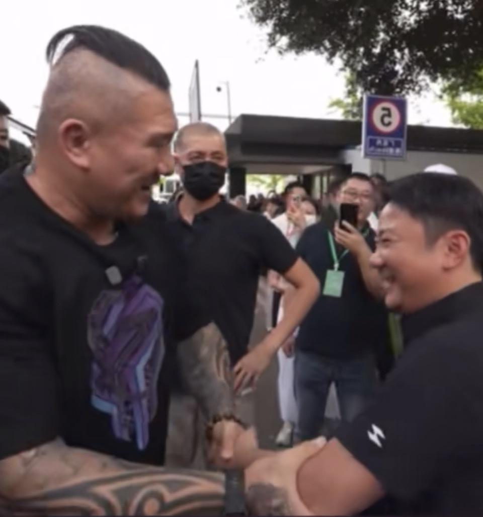 两个大汉在街头握手，周围围着一群人。英雄聚首，共话天下事。