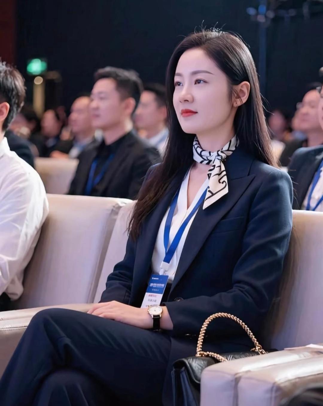 会场的顶灯漫过前排的椅背，落在丝巾的黑白纹路里，漾成细碎的光。西装的肩线撑着恰到