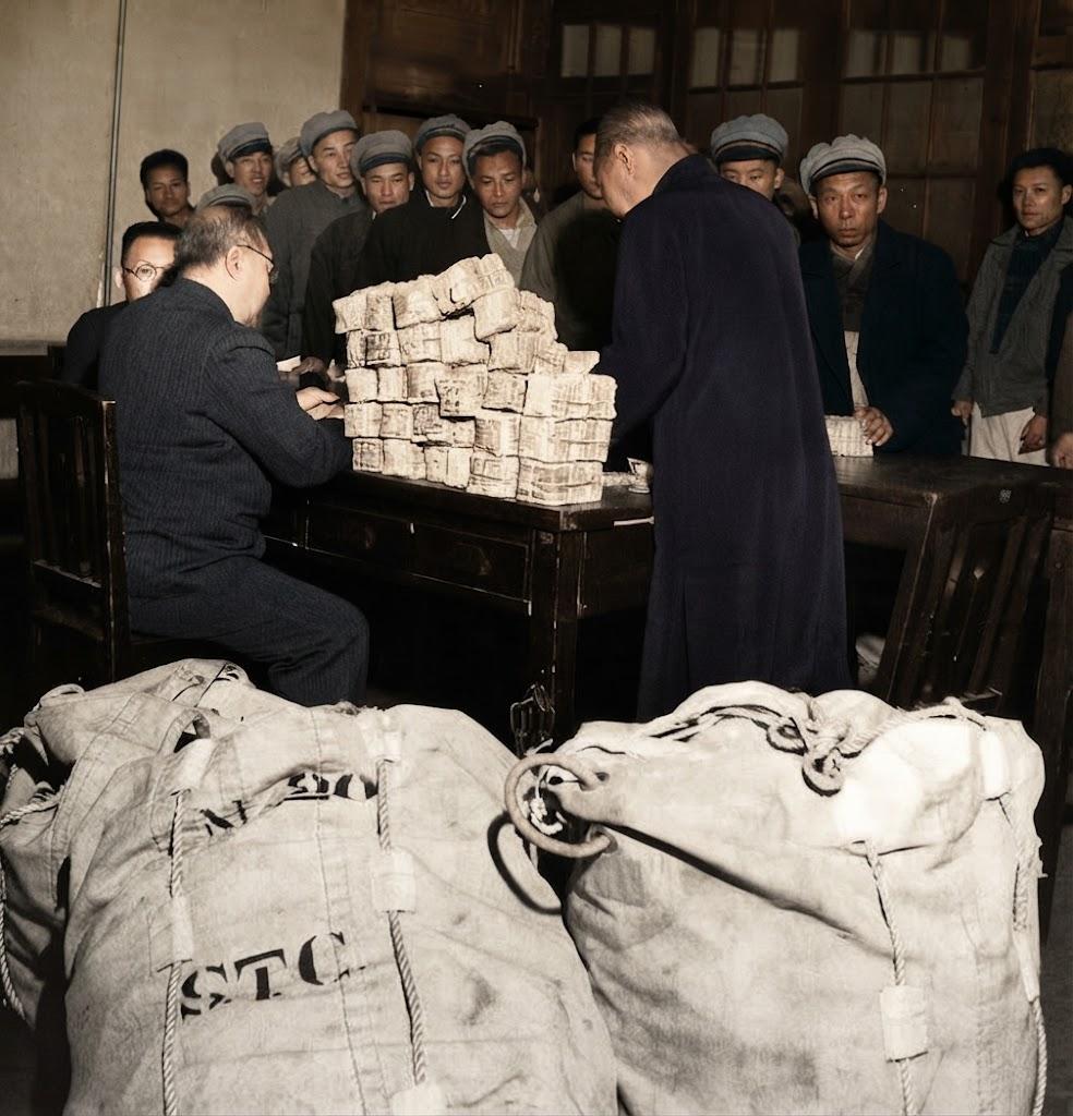 1948年3月，上海。银行正向上海电力公司职工发放工资，桌上堆叠着成百上千捆纸币