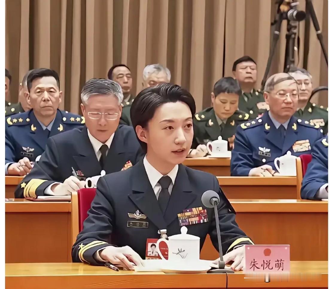 她在发言席上发言，背后将星云集。她是辽宁舰第一批女舰员，曾是全舰唯一女基层主官。