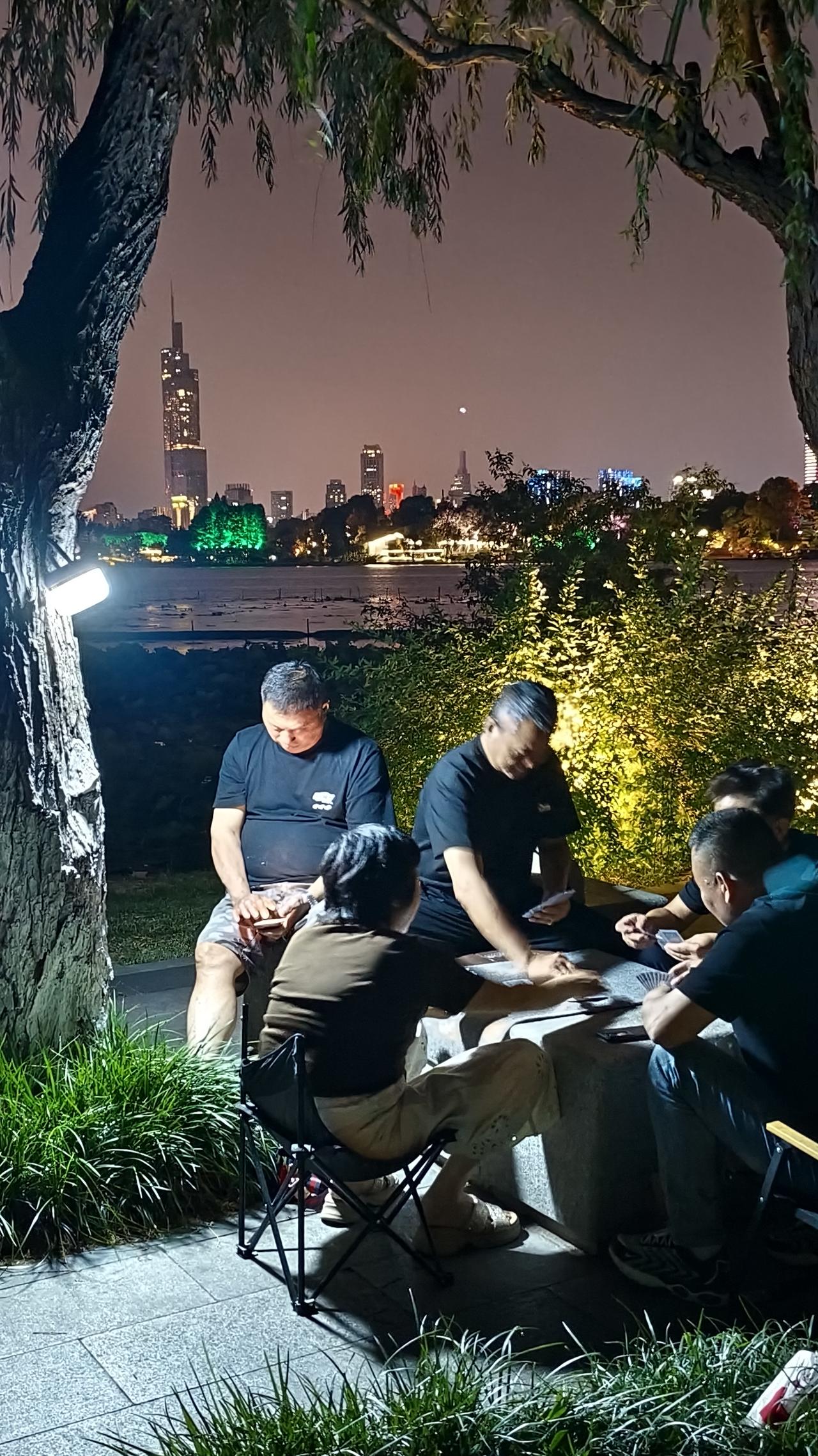 《紫峰大厦为背景，玄武湖夜牌局开始了》
    南京人的夏夜，一半是玄武湖的晚风