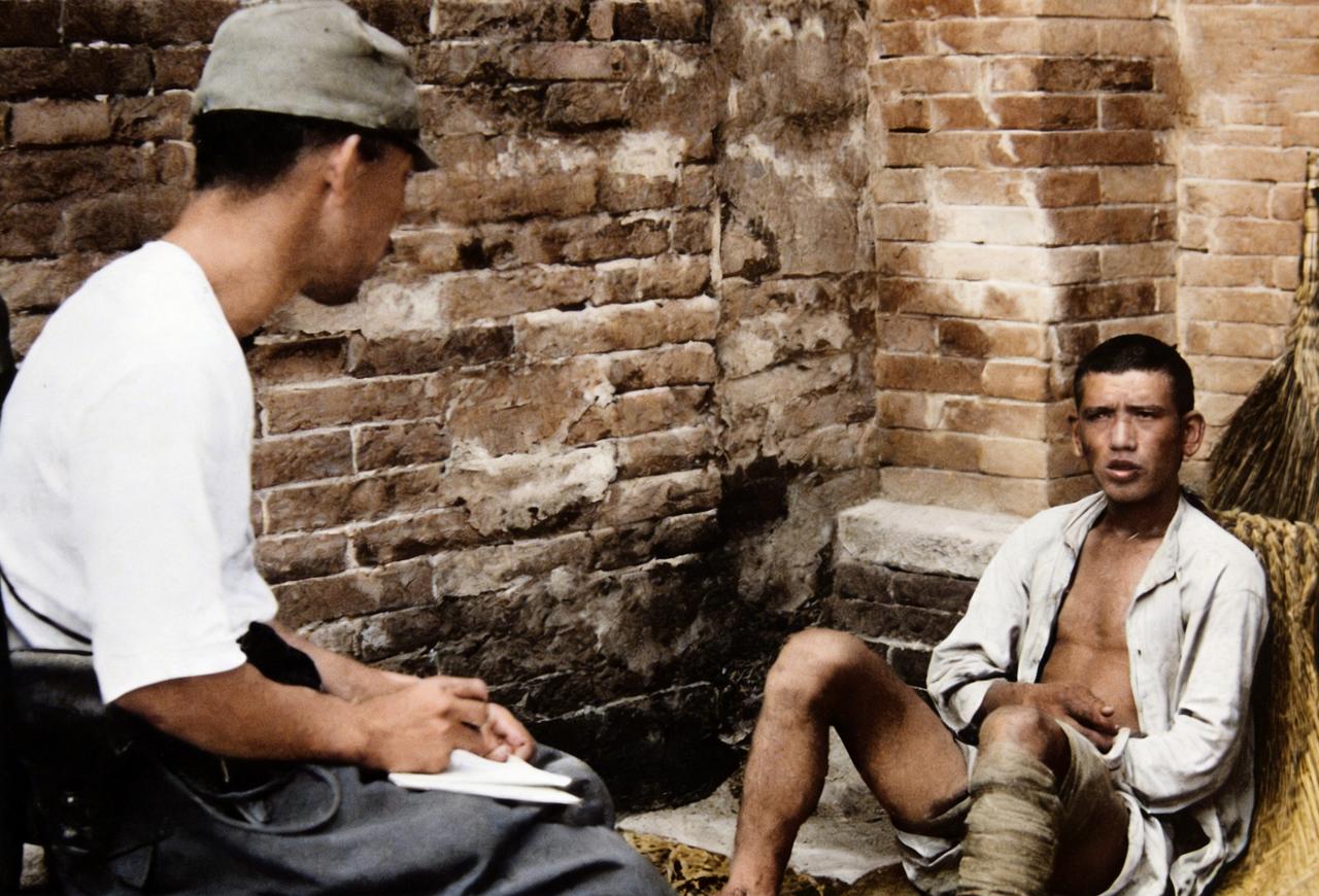 这是抗战时一名日寇在审讯一名被俘虏的中国年轻士兵。面对日寇的审讯，年轻士兵靠在后