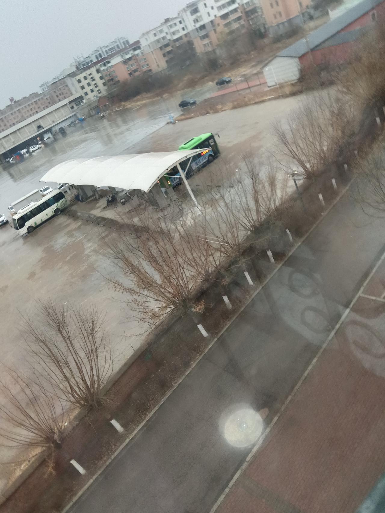 雨中城市一角，公交车停靠在雨棚下，静待归人。