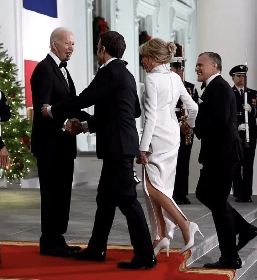 一身白裙的布吉丽特，美的像人见人爱的小仙女。
马克龙对她爱不释手，拜登热情的搂着