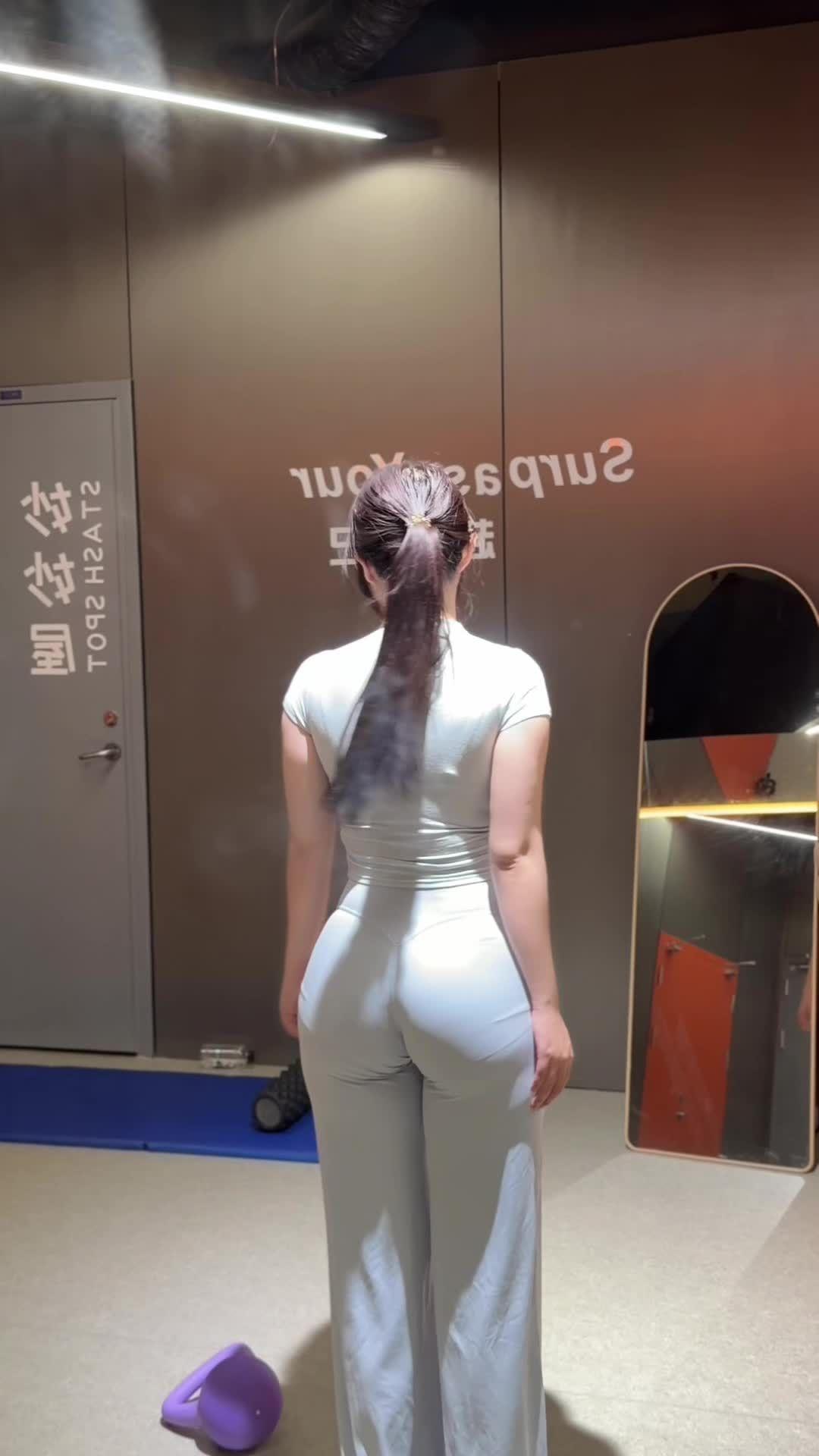 一个穿紧身衣的女士站在镜子前。