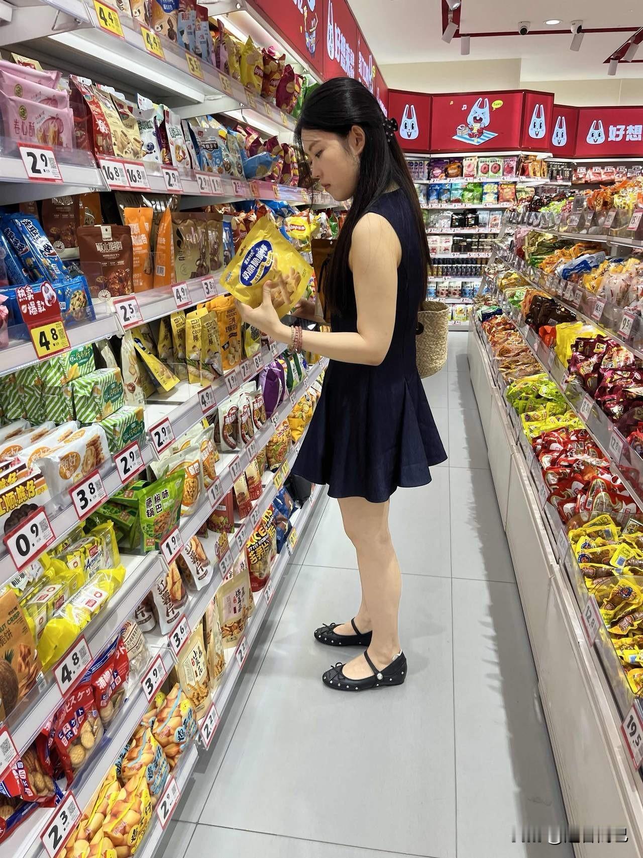 美女在超市货架前认真挑选零食。