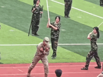 军人教官让众多女学生用木条打击他的身体，他站立不动抗击打的能力实在太强。