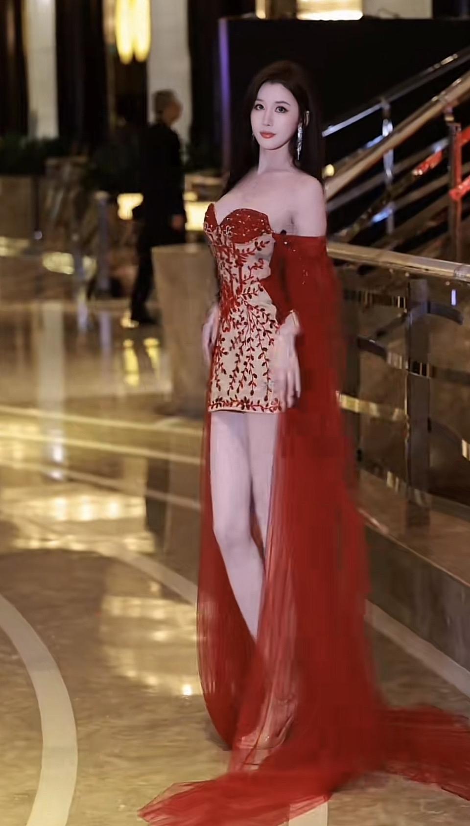 这位女士穿着红色晚礼服，站在楼梯旁。