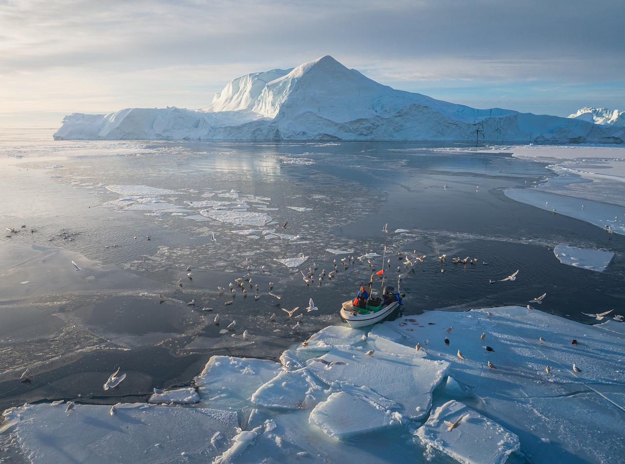 格陵兰岛西海岸的伊卢利萨特冰湾，一艘小型渔船停泊在浮冰与开阔水域交界处，周围环绕
