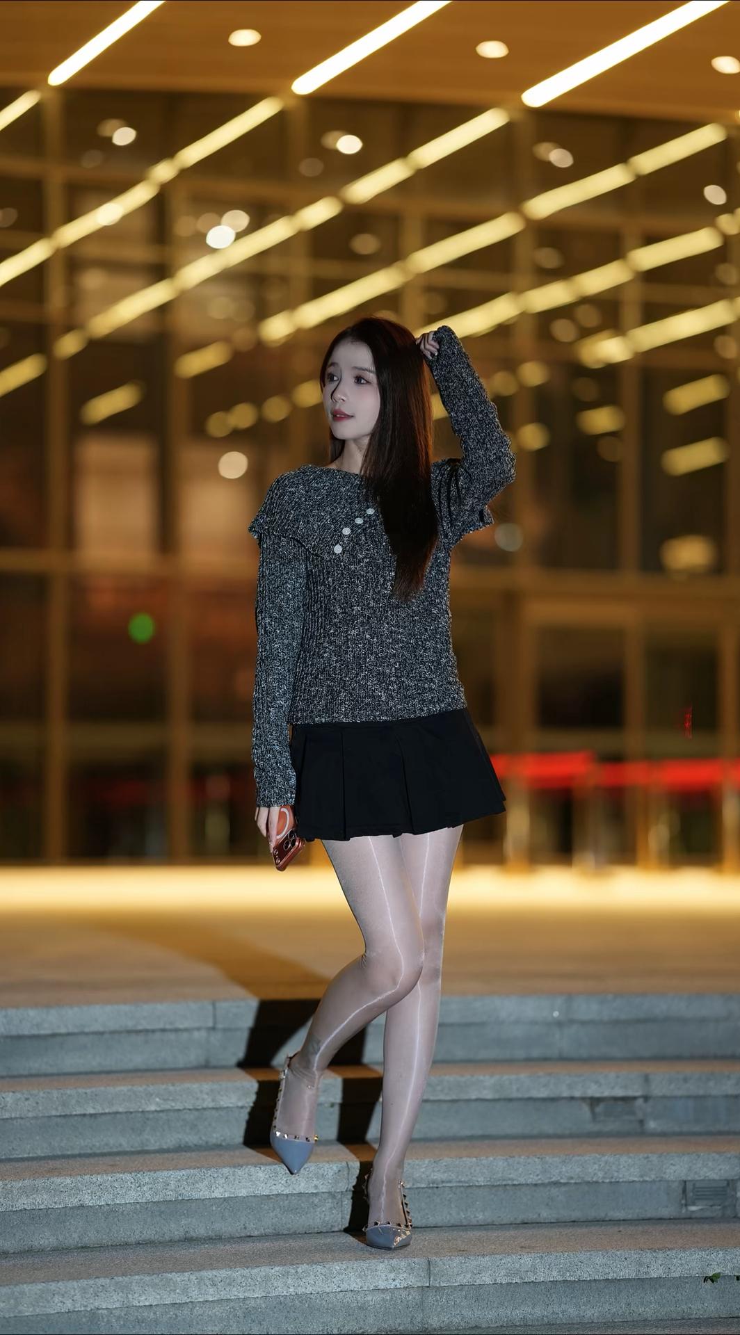 画面中，一位年轻女性立于夜晚的户外场景。她留着一头柔顺的棕色长发，发丝自然垂落在