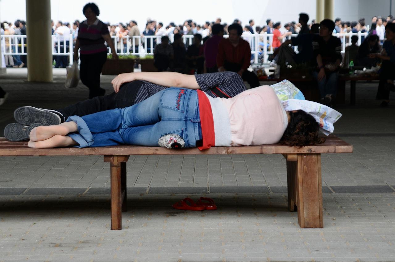 一位衣着得体的女孩子旁若无人地躺卧在路边的长椅上。在车站、机场、商超、公园、旅游
