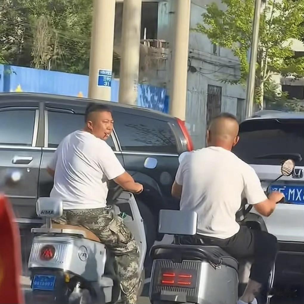 网友在街头偶遇东北雨姐，只见雨姐骑着爱玛电动车，嘴里叼着烟，与旁边人交流，依然霸
