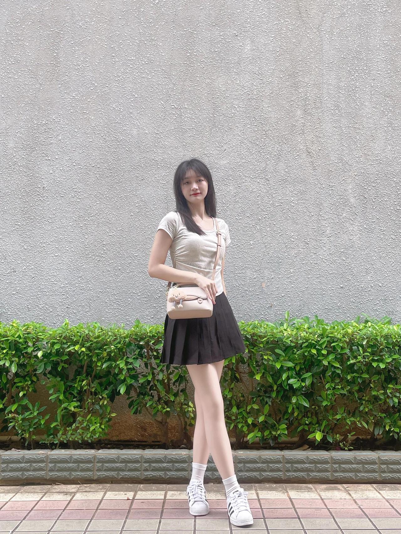 女生上身着浅灰紧身短T，显纤细身姿;下装黑色百褶短裙，灵动俏皮。白色运动鞋与短袜