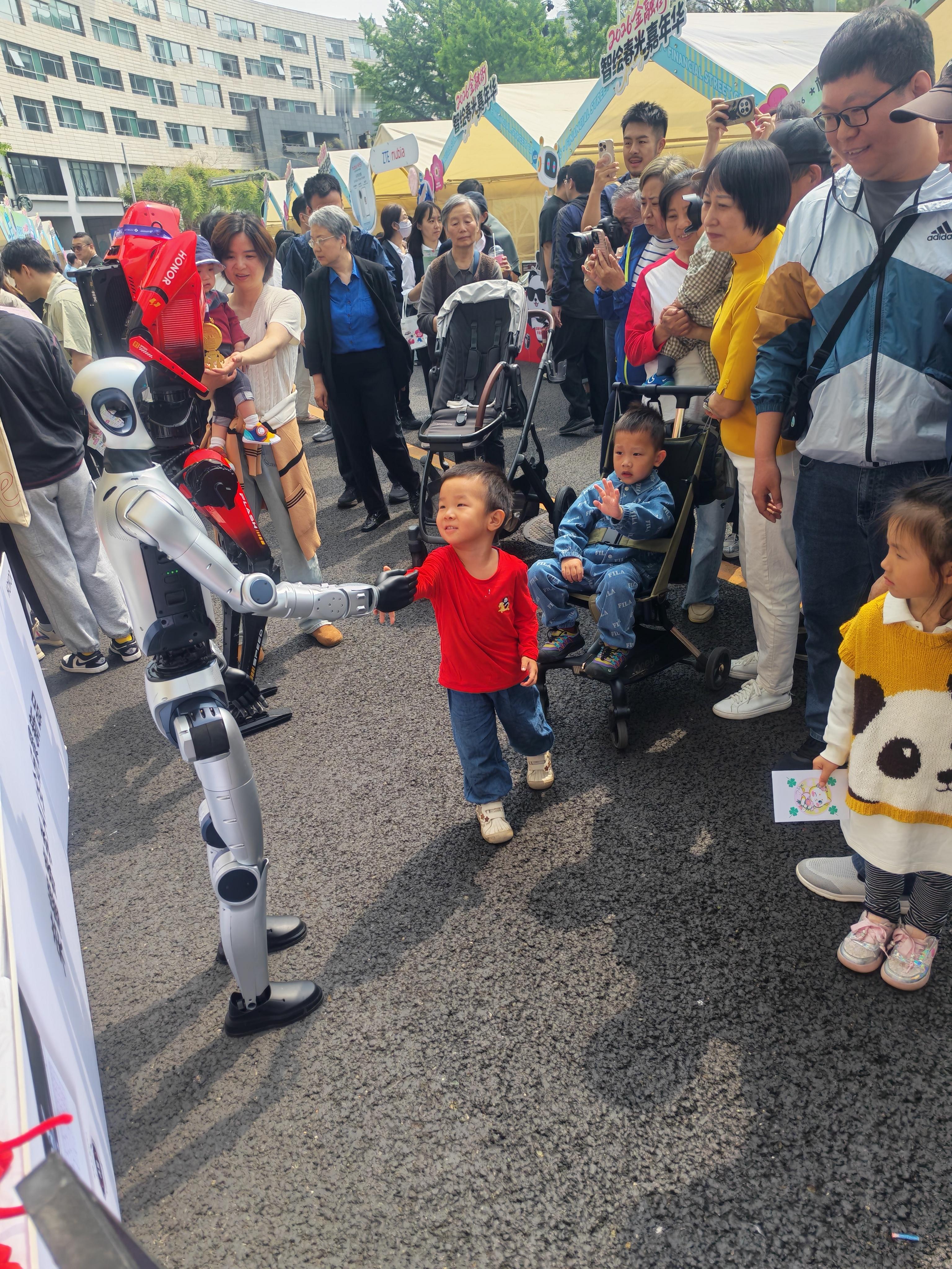 荣耀机器人夺冠后首次亮相2026金融街智绘春光嘉年华看到荣耀机器人和小朋友互动，