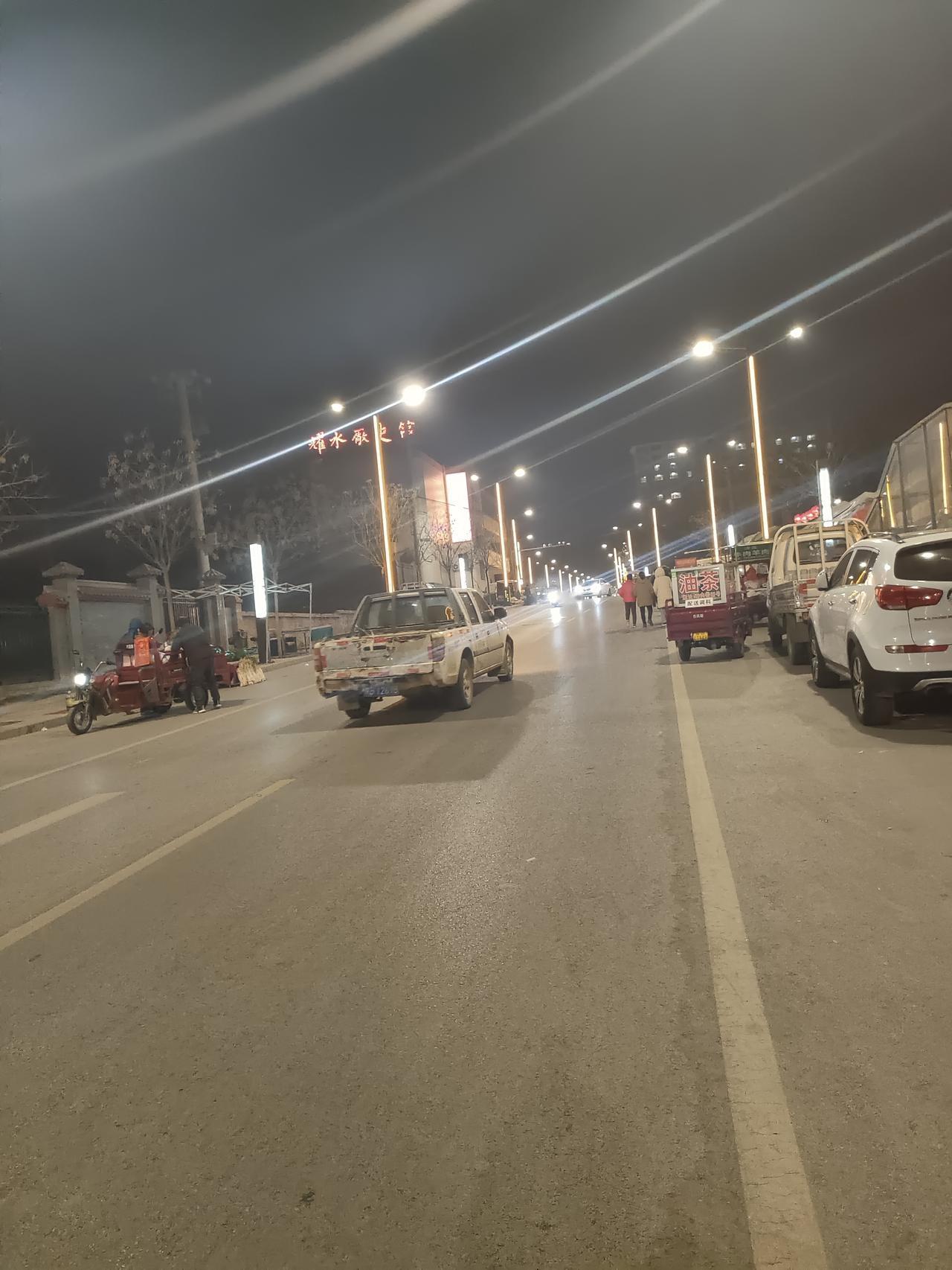 路灯把光的丝线抛向夜空，车辆与行人在暖黄里游移，这夜的街道，正把烟火气熬成温柔的