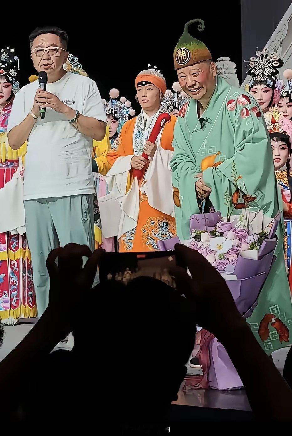 于谦和身着戏曲戏服扮丑角的郭德纲演出后与一众演员们谢幕时的留影，于谦致辞，台下许