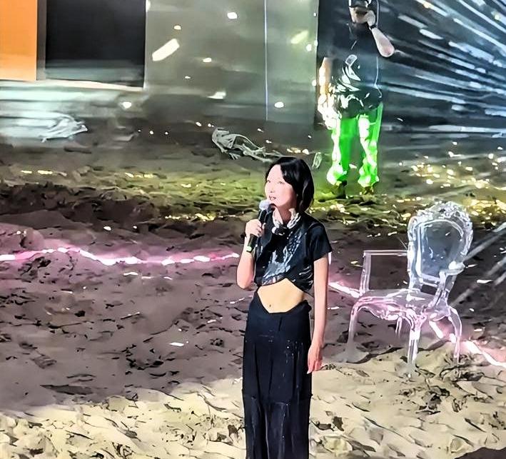 周冬雨站在话剧舞台中央，灯光打在她脸上。她嘴在动，眼睛一直往右上方瞟。提词器的绿
