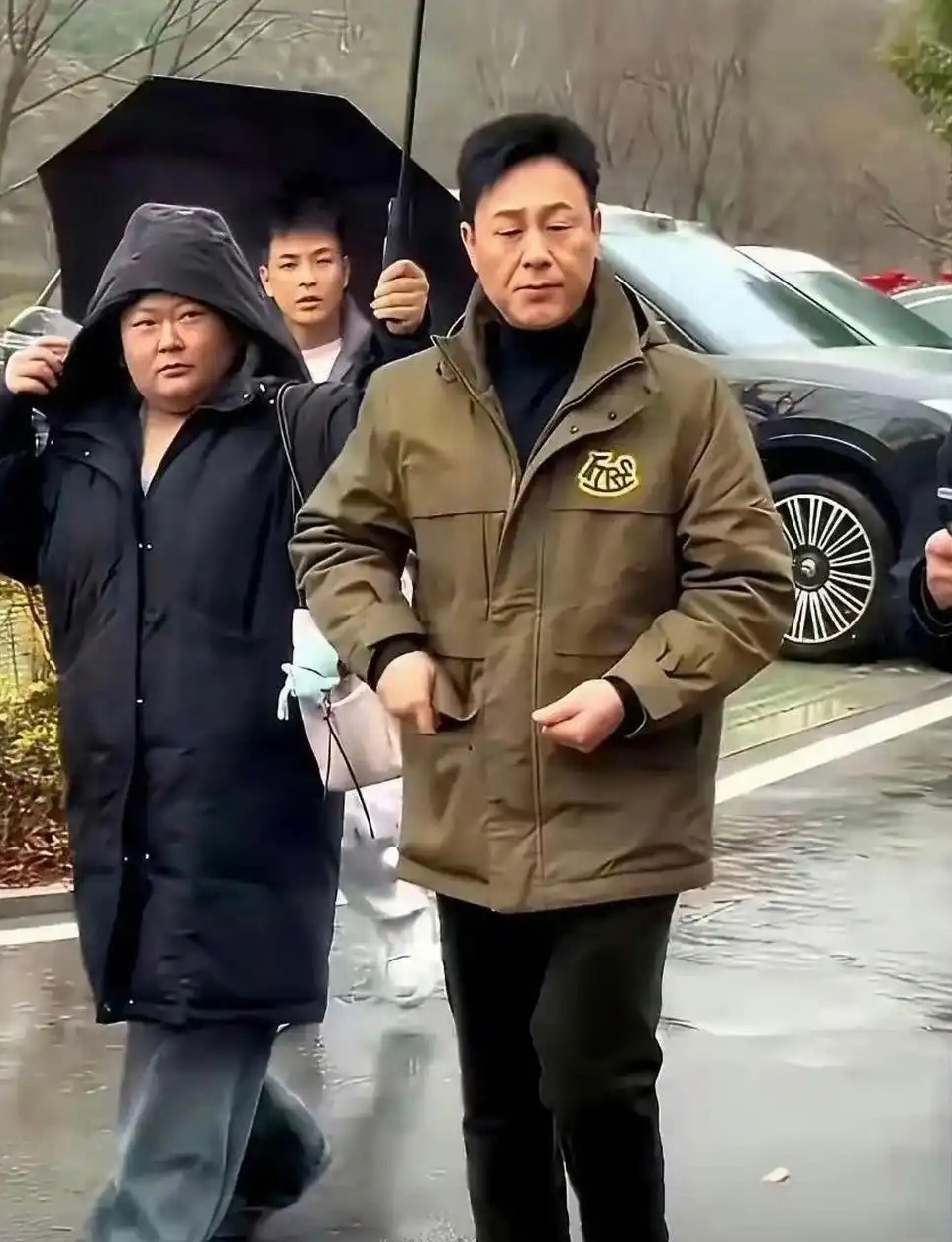 女助理半个身子都在淋着雨，张颂文还在伞下悠闲的嗑瓜子 